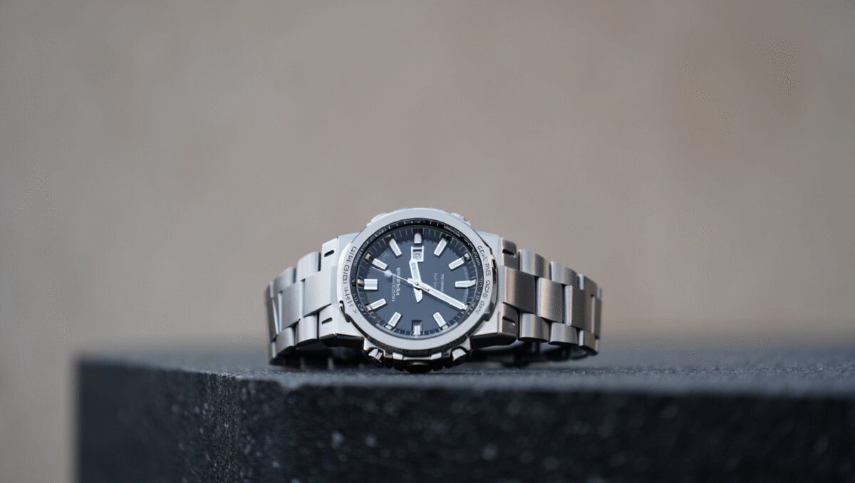 Close-up of a silver metal wristwatch side showing two push buttons, a crown, and screws on a black background.