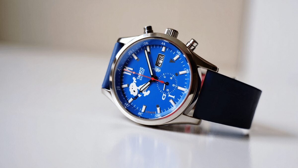 Silver metal wristwatch with a dark blue tachymeter bezel and black dial featuring three subdials and silver markers.