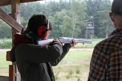 Safety glasses and a clay target on a table with a blurred shotgun silhouette