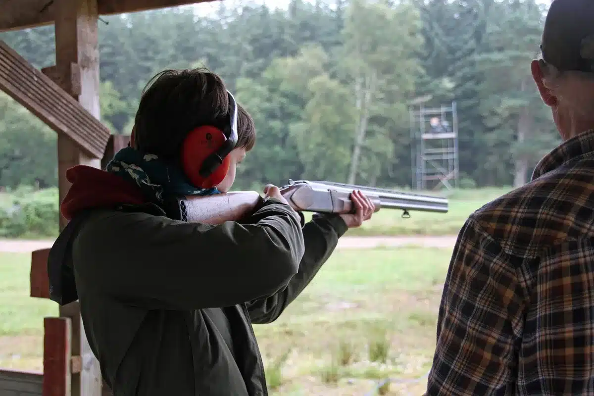 Safety glasses and a clay target on a table with a blurred shotgun silhouette