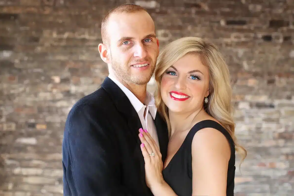 Black-and-white style photo of a smiling couple showing an engagement ring