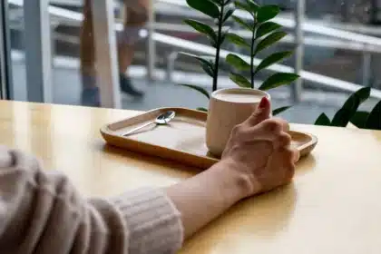 Two anonymous hands holding a coffee mug over a breakfast table with pancakes