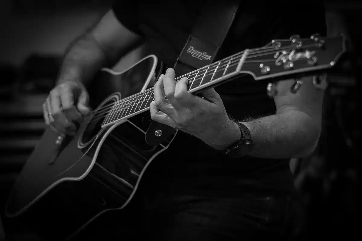 Close-up of hands playing an acoustic guitar with pedal steel in background