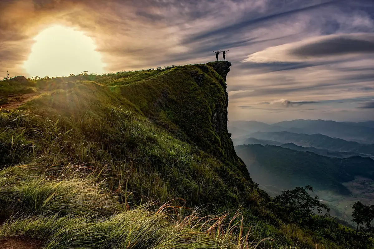 Silhouetted climbers and prayer flags on a high mountain ridge at dawn