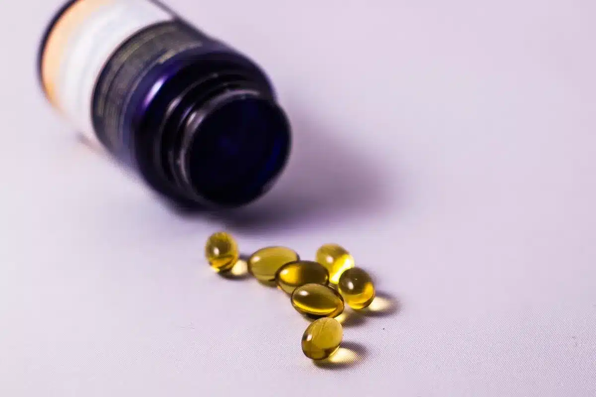 Open bottle of omega-3 softgels on a kitchen counter with a glass of water