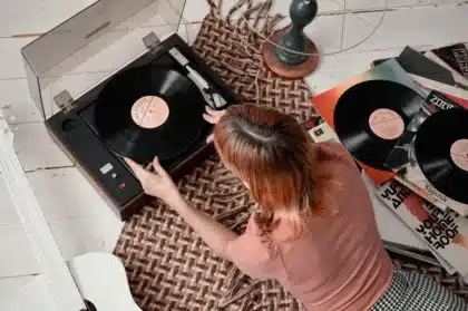 Folded newspaper on carpeted stairs next to a vintage vinyl player and anonymous hands